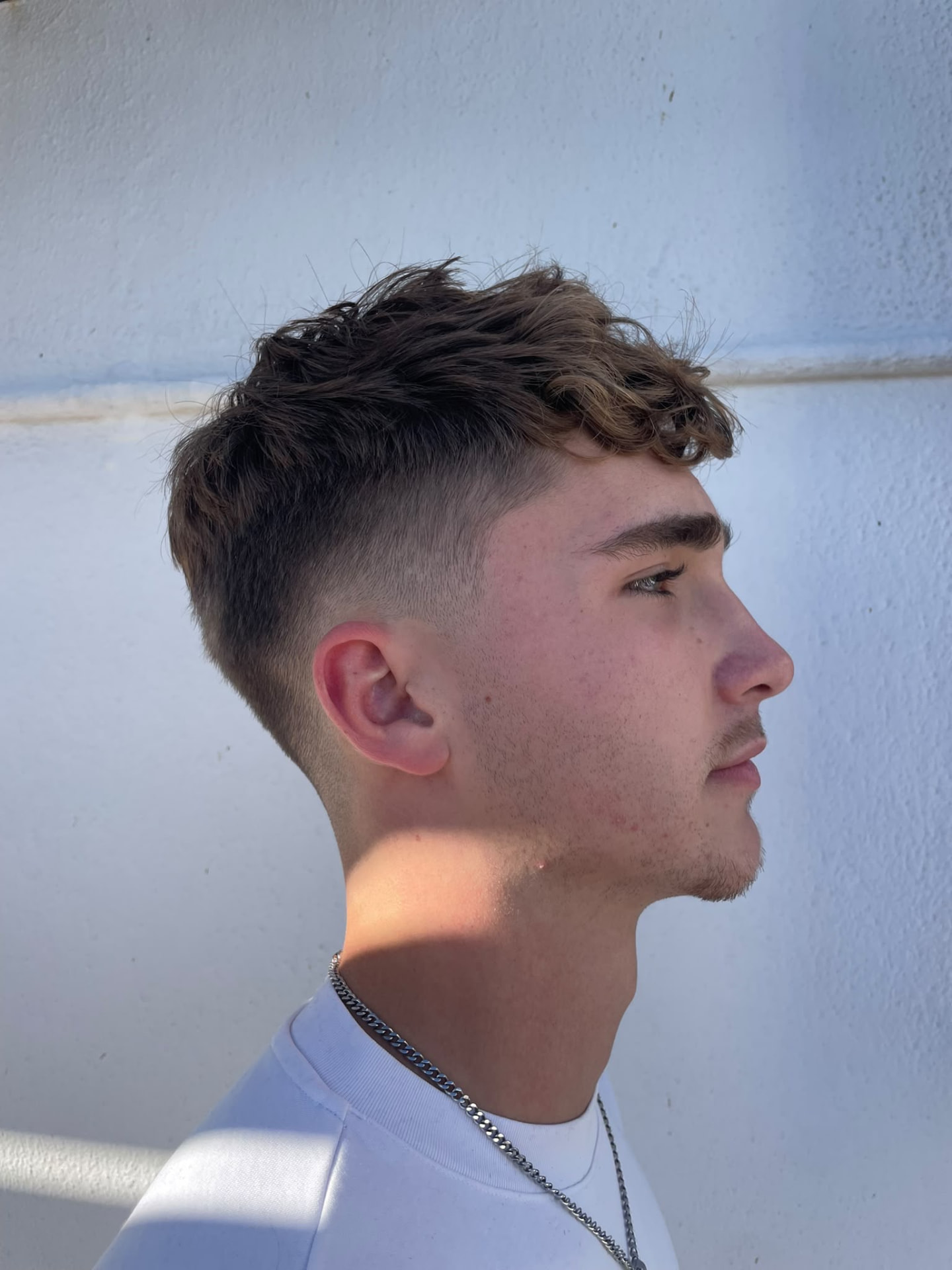 A fresh skin-fade men's cut with a curly textured top, side profile