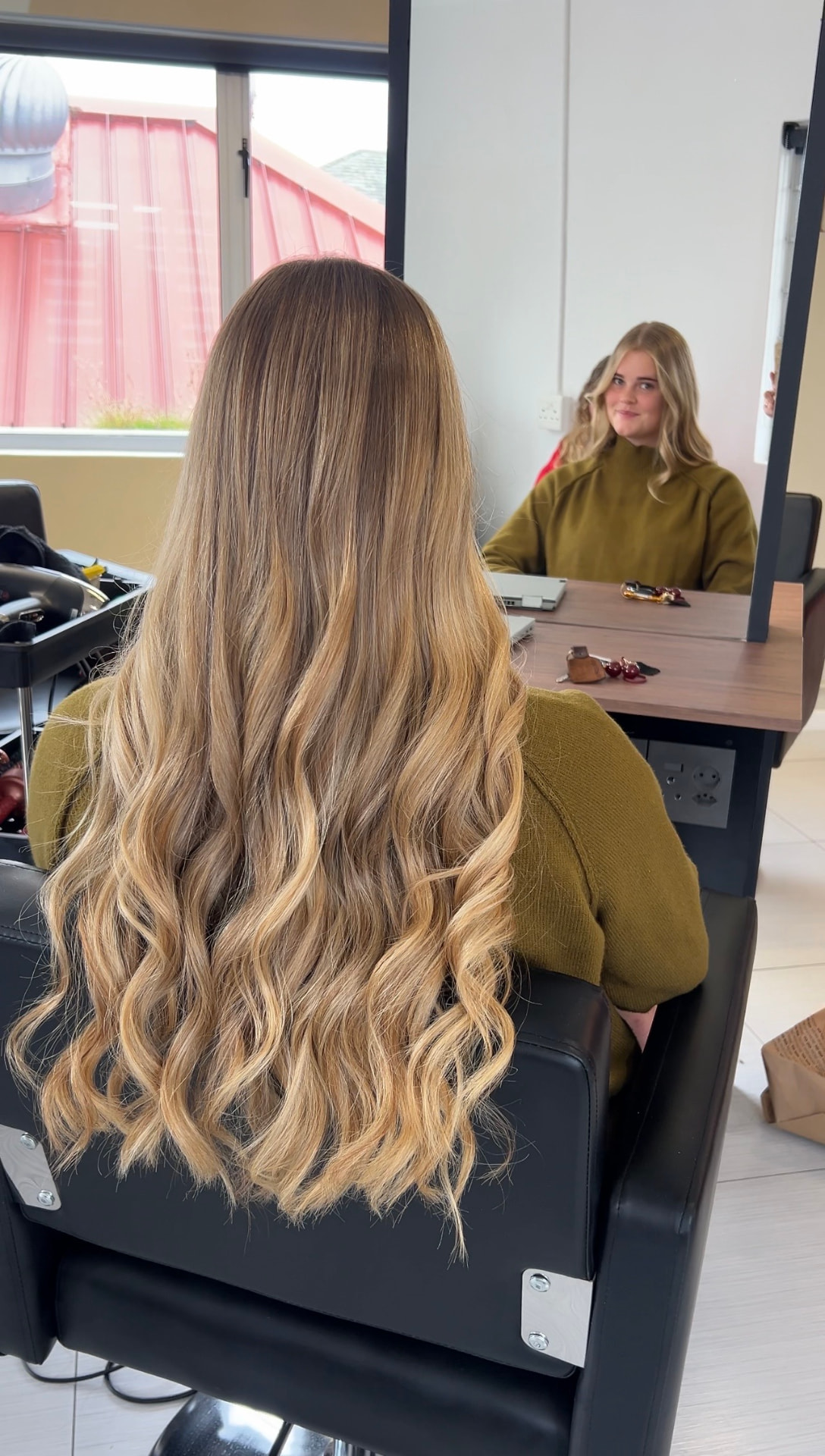 Long wavy blonde extensions styled in soft curls, seen from behind in the studio